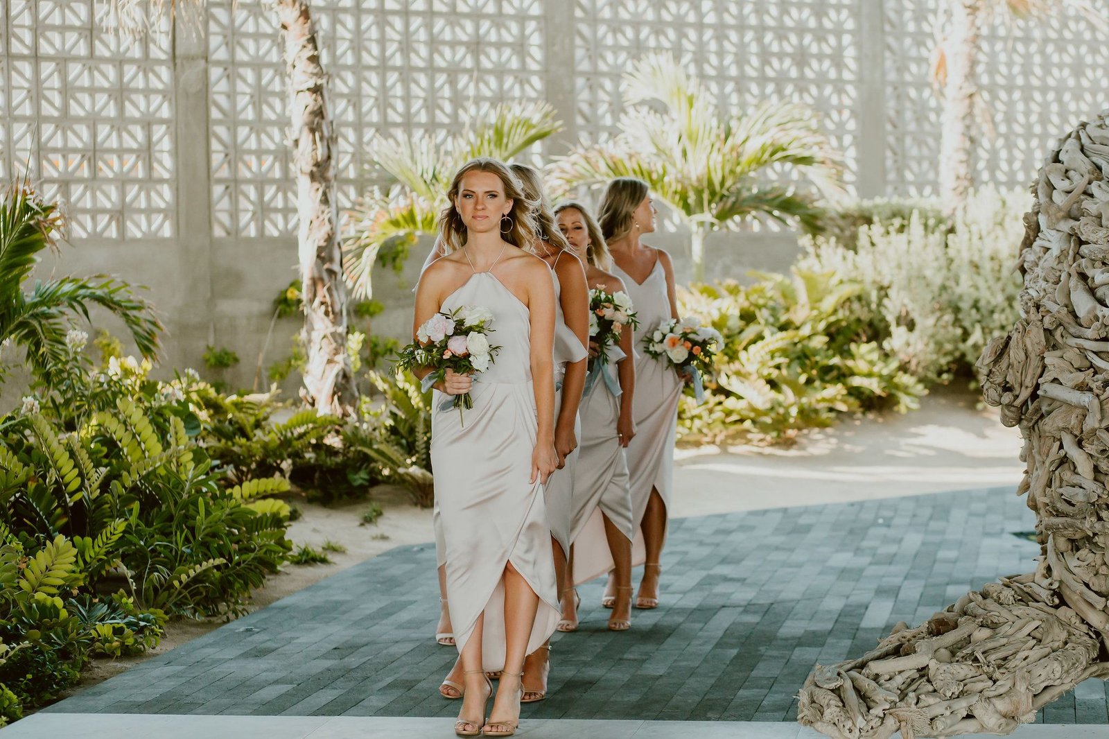 Bridesmaids walking down the aisle with their beautiful bouquets designed by Lola from Florenta Design. Photo was taken by Ana and Jerome Photography at The Cape Los Cabos, by Thompson Hotels