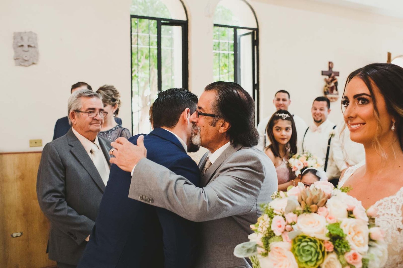 The father of the Bride is hugging the Groom as he hands his daughter off. This wedding was at the Evangelist Church in Los Cabos Mexico. 