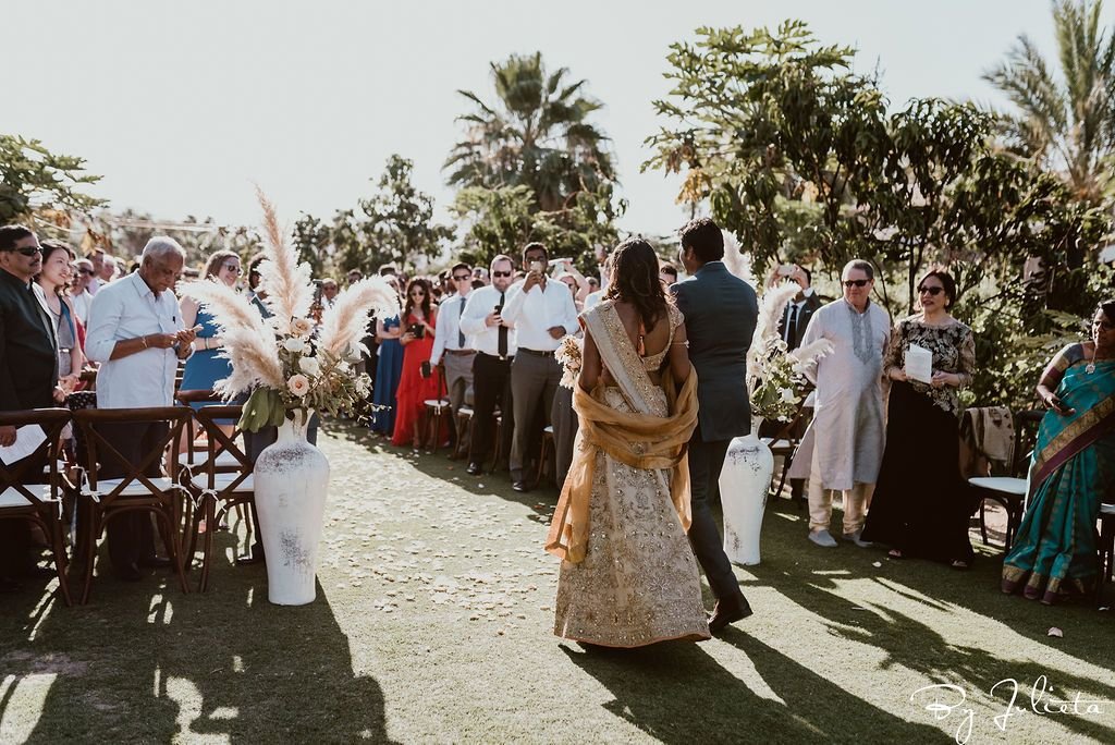 Bride walking down the aisle to her wedding ceremony with her brother in her arm. This Wedding Venue was Flora Farms in Los Cabos, Mexico.