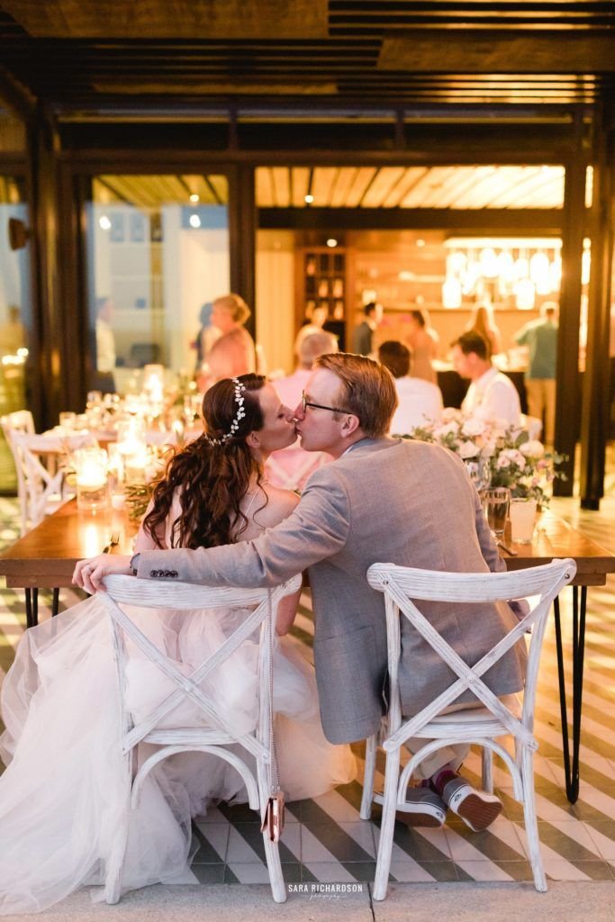 Bride and Groom kissing at their Sweetheart Table as Guests aligned their glasses with their forks for the Bride and Groom to Kiss. This photo was taken by Sara Richardson at The Cape in Los Cabos Mexico