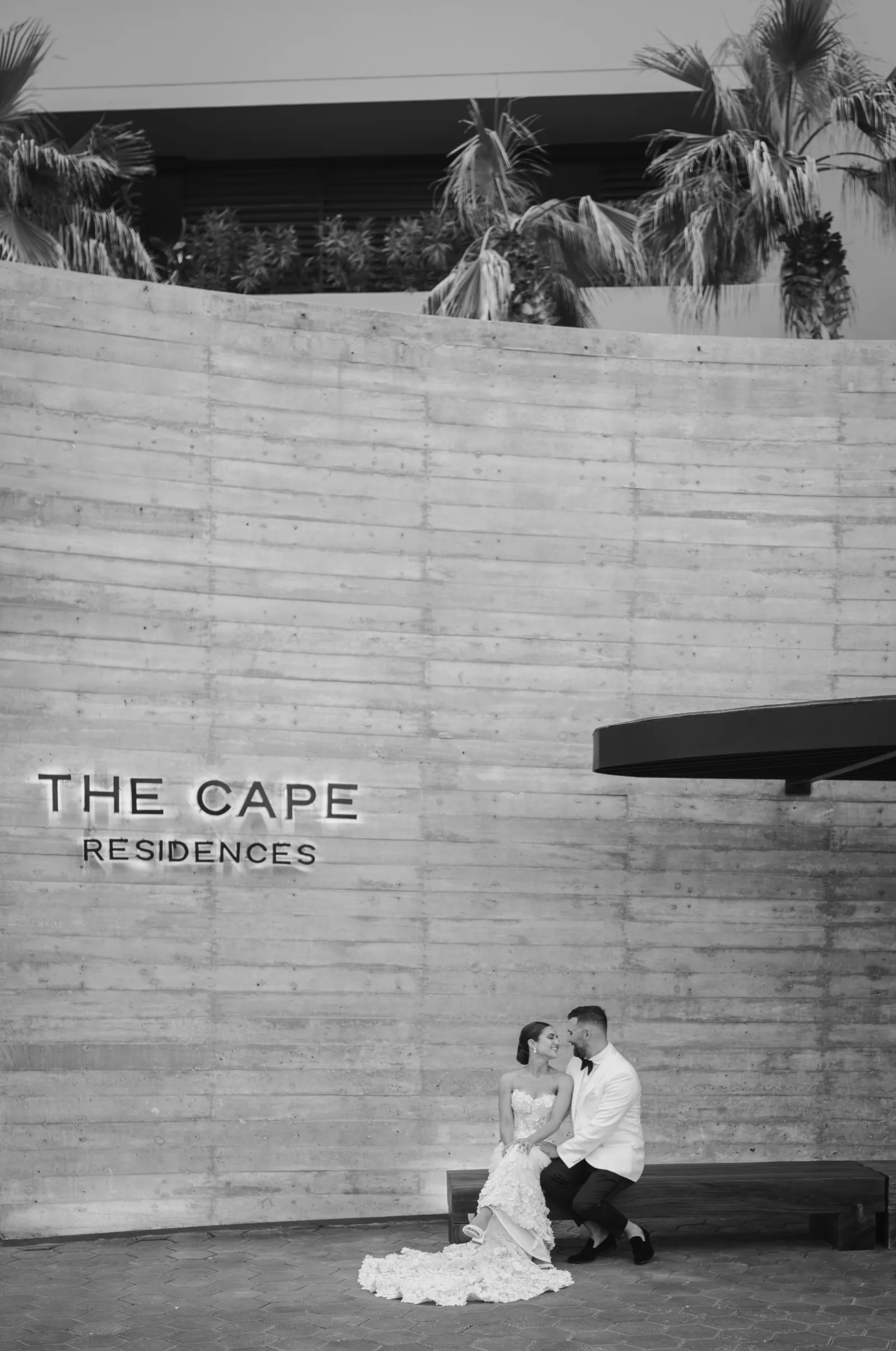Couple seated below The Cape Residences sign in Cabo San Lucas
